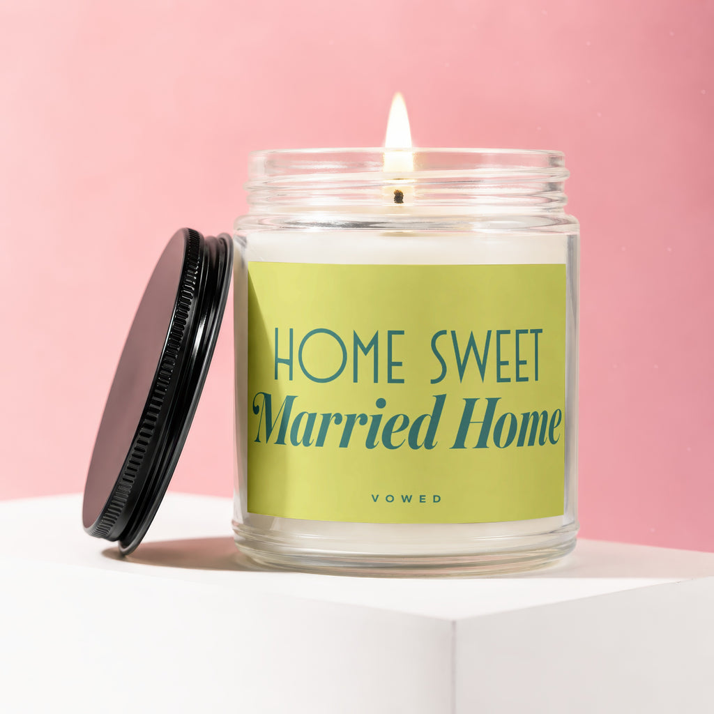 Lit candle in glass jar with green label reading "HOME SWEET Married Home VOWED".