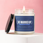 Glass jar candle with lit flame and blue label reading "HE MARRIED UP".
