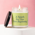 Candle with lid removed, lit wick, and label saying "A Spark for Our New Beginning".