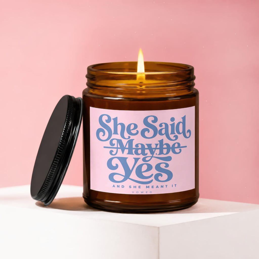 Amber candle with pink label reading "She Said Maybe Yes And She Meant It Vowed".