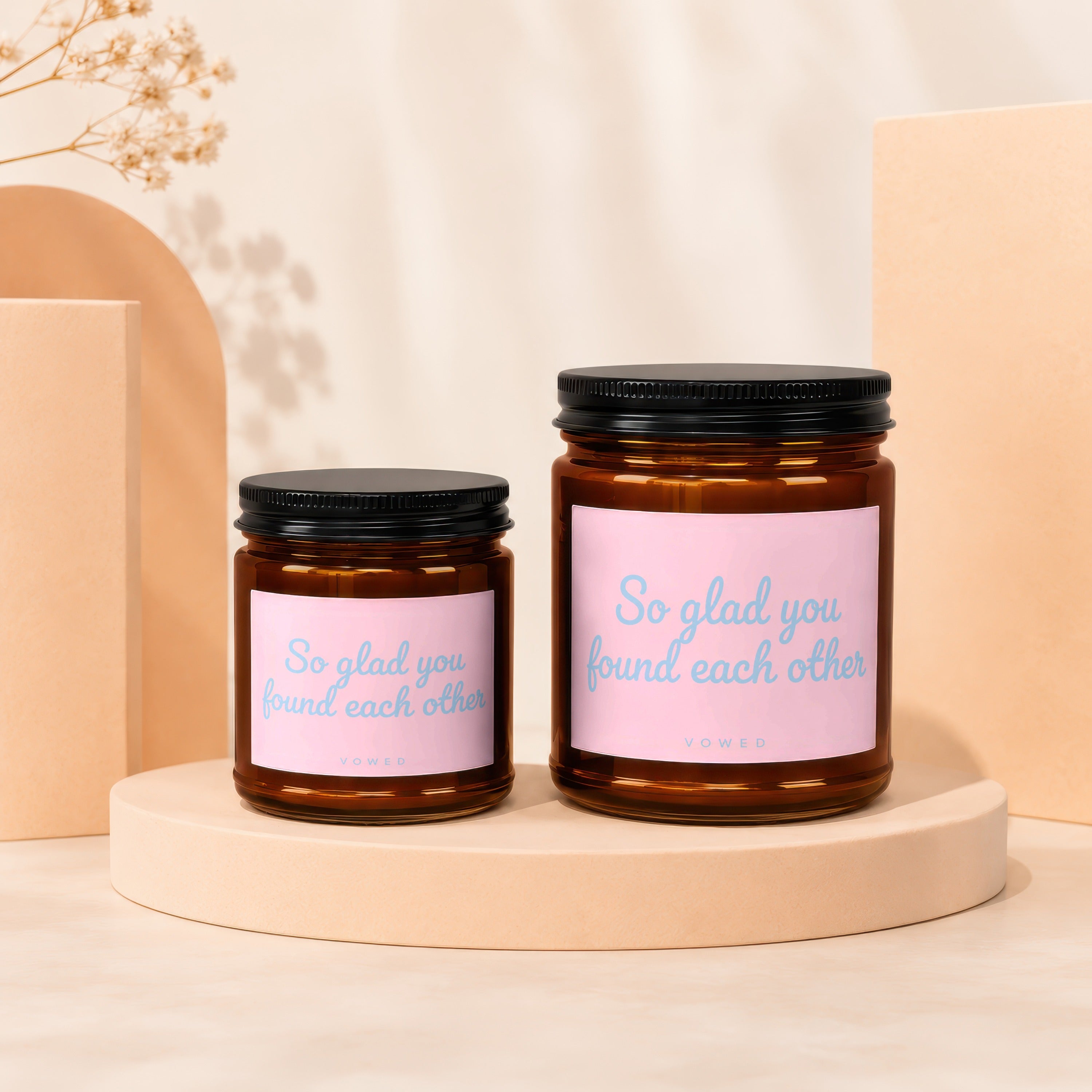 Two amber glass candles with pink labels reading "So glad you found each other" and "VOWED".