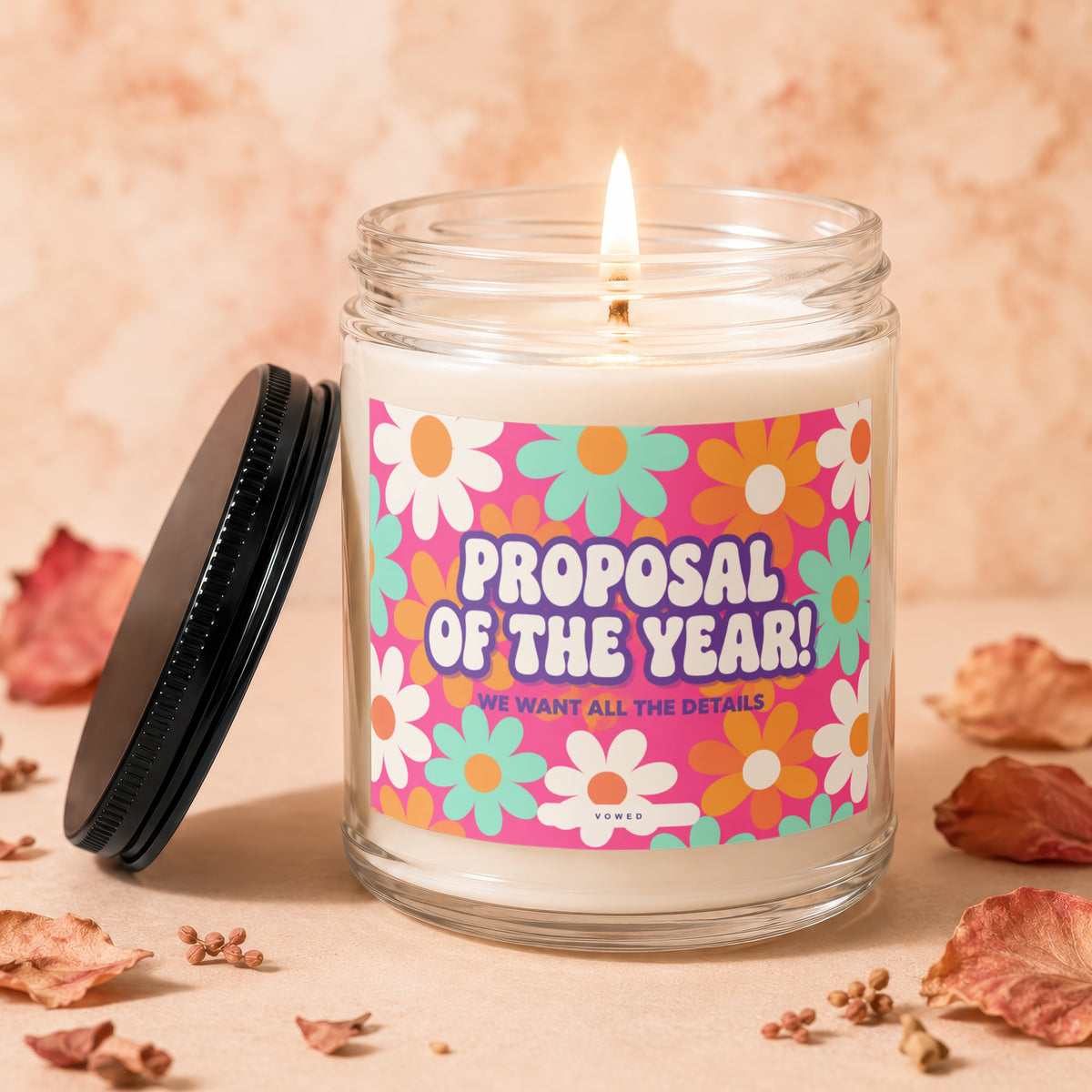 Glass candle with lit flame, floral label reading "Proposal of the Year!"