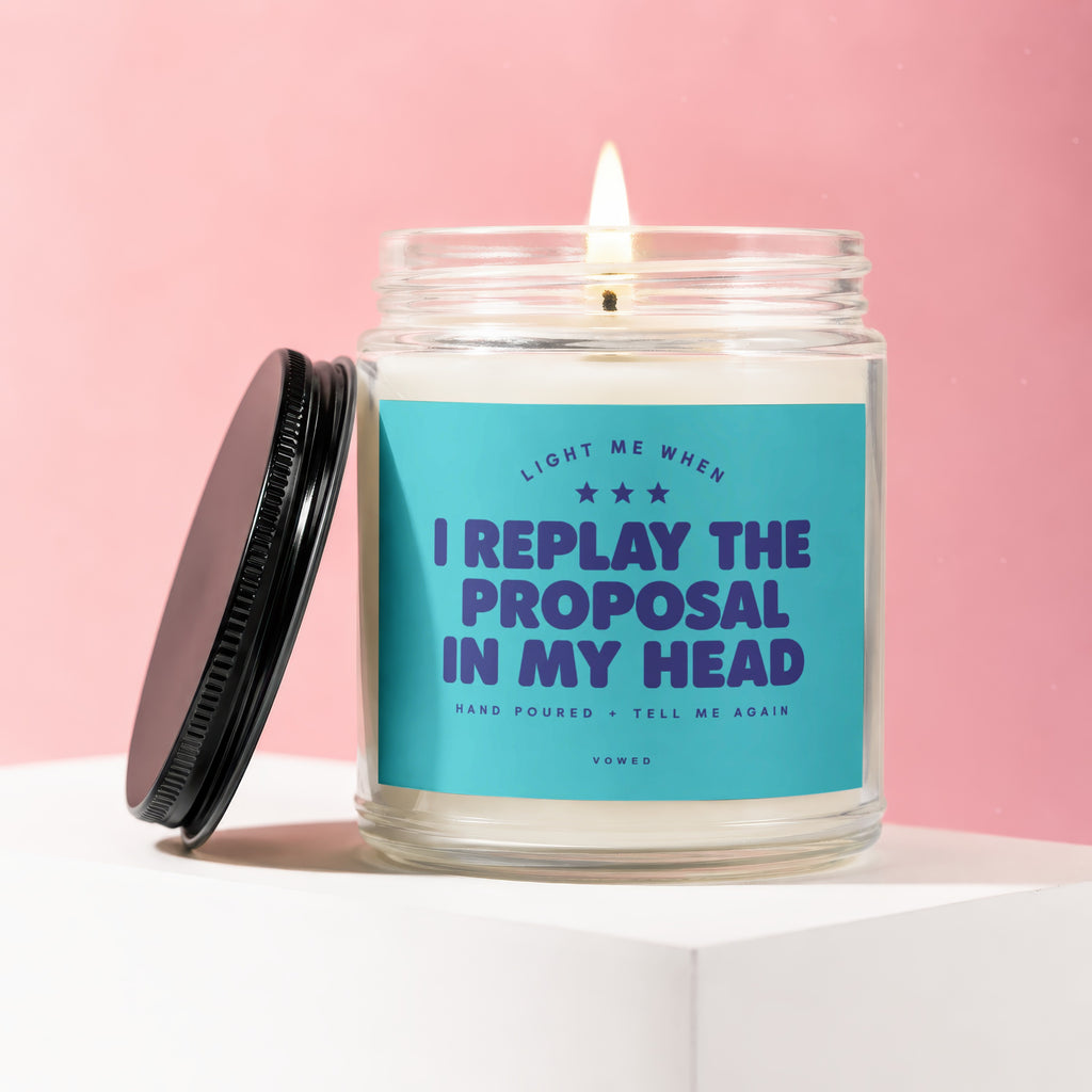 Glass candle with teal label reading "I replay the proposal in my head."