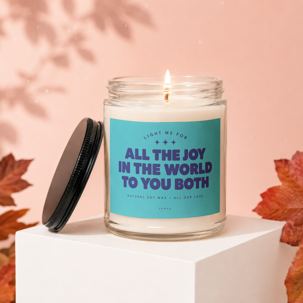 Burning candle in glass jar with "All The Joy In The World To You Both" text.