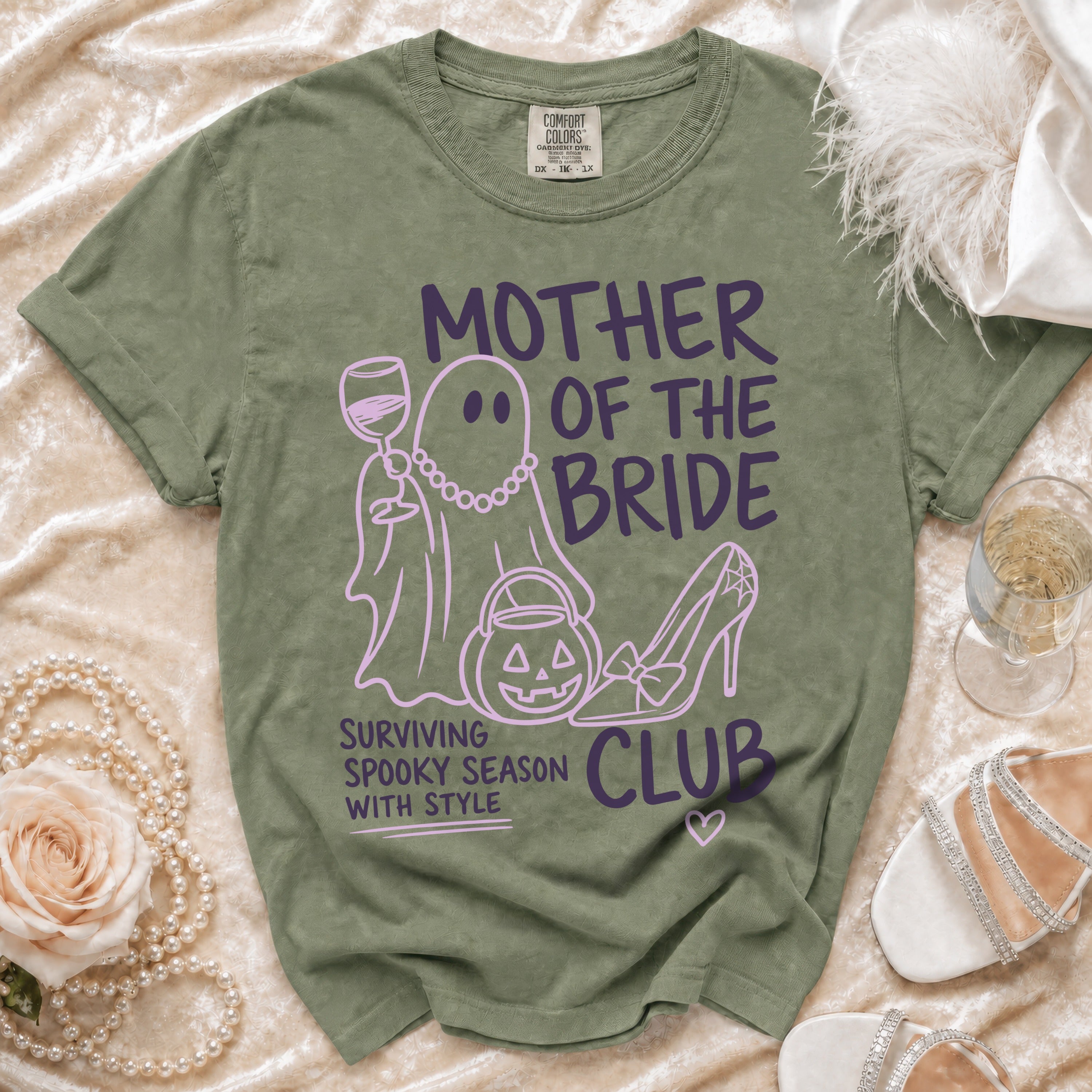 Green t-shirt with purple text and graphics reading "MOTHER OF THE BRIDE" and "SURVIVING SPOOKY SEASON WITH STYLE".