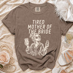 T-shirt with "Tired Mother of the Bride" text and graphic, surrounded by decorative items.
