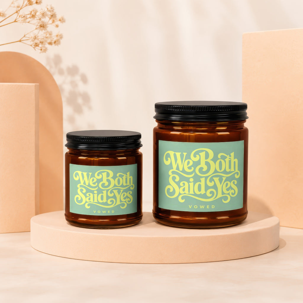 'We Both Said Yes' inscribed on two amber glass jar candles with black lids.