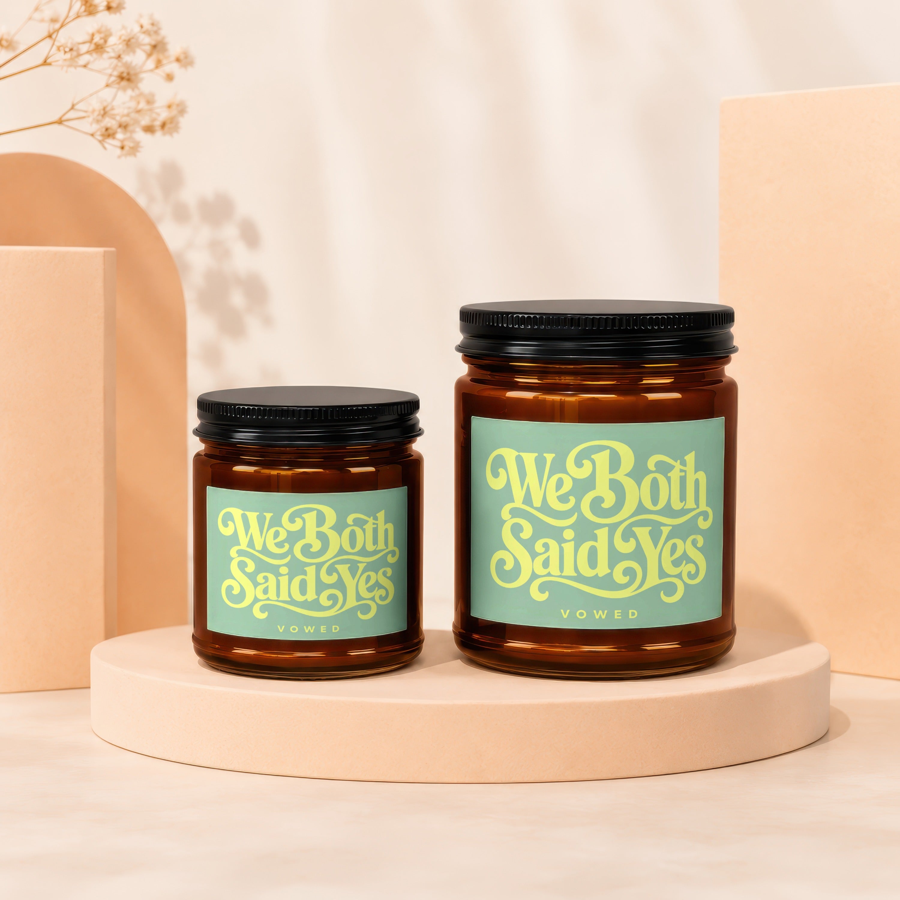 'We Both Said Yes' inscribed on two amber glass jar candles with black lids.