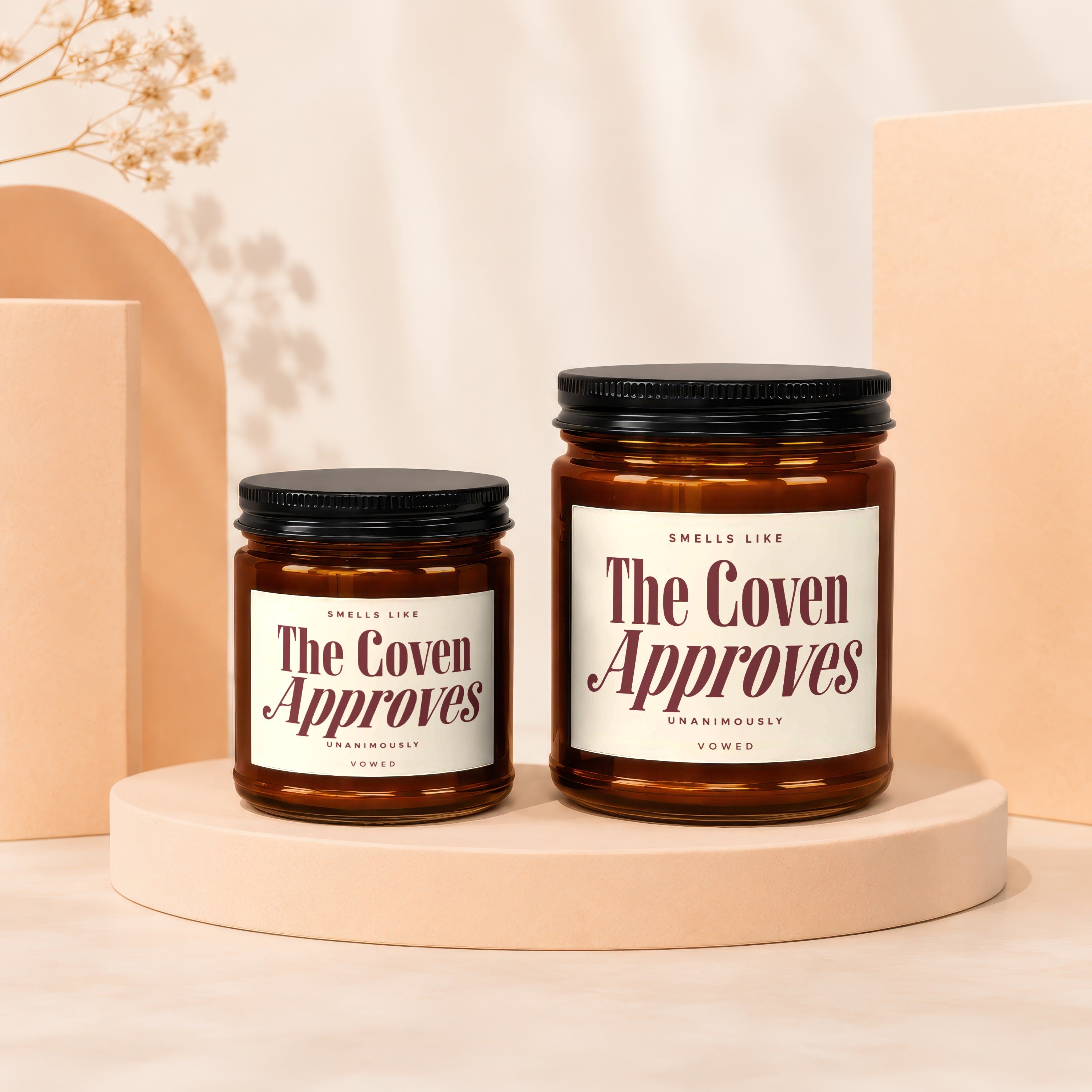 Two amber glass candles labeled "The Coven Approves" with black lids.