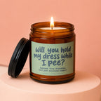 Amber jar candle with lit wick, label reads "will you hold my dress while I pee?"