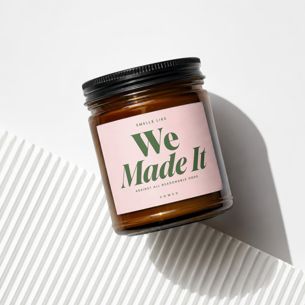 Amber jar candle with pink label reading "Smells Like We Made It"