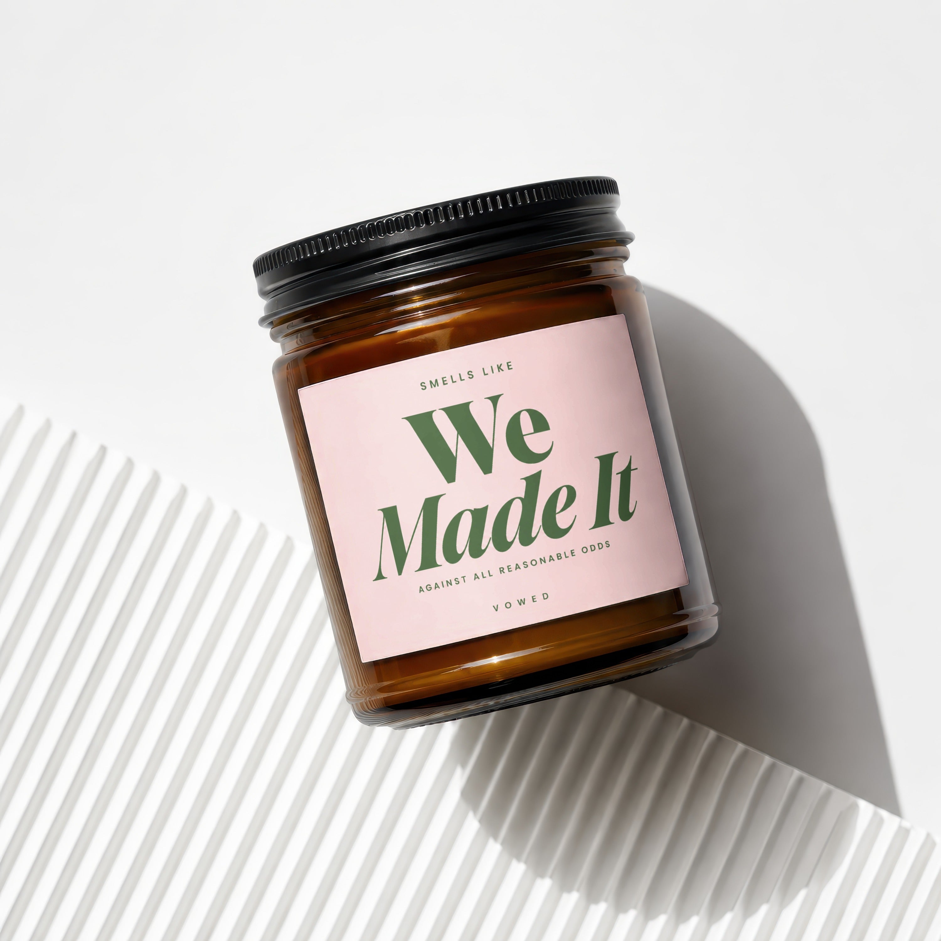 Amber jar candle with pink label reading "Smells Like We Made It"