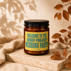 Amber candle with black lid, yellow label reading "WELCOME TO THE GROUP PROJECT WEDDING PARTY VOWED".
