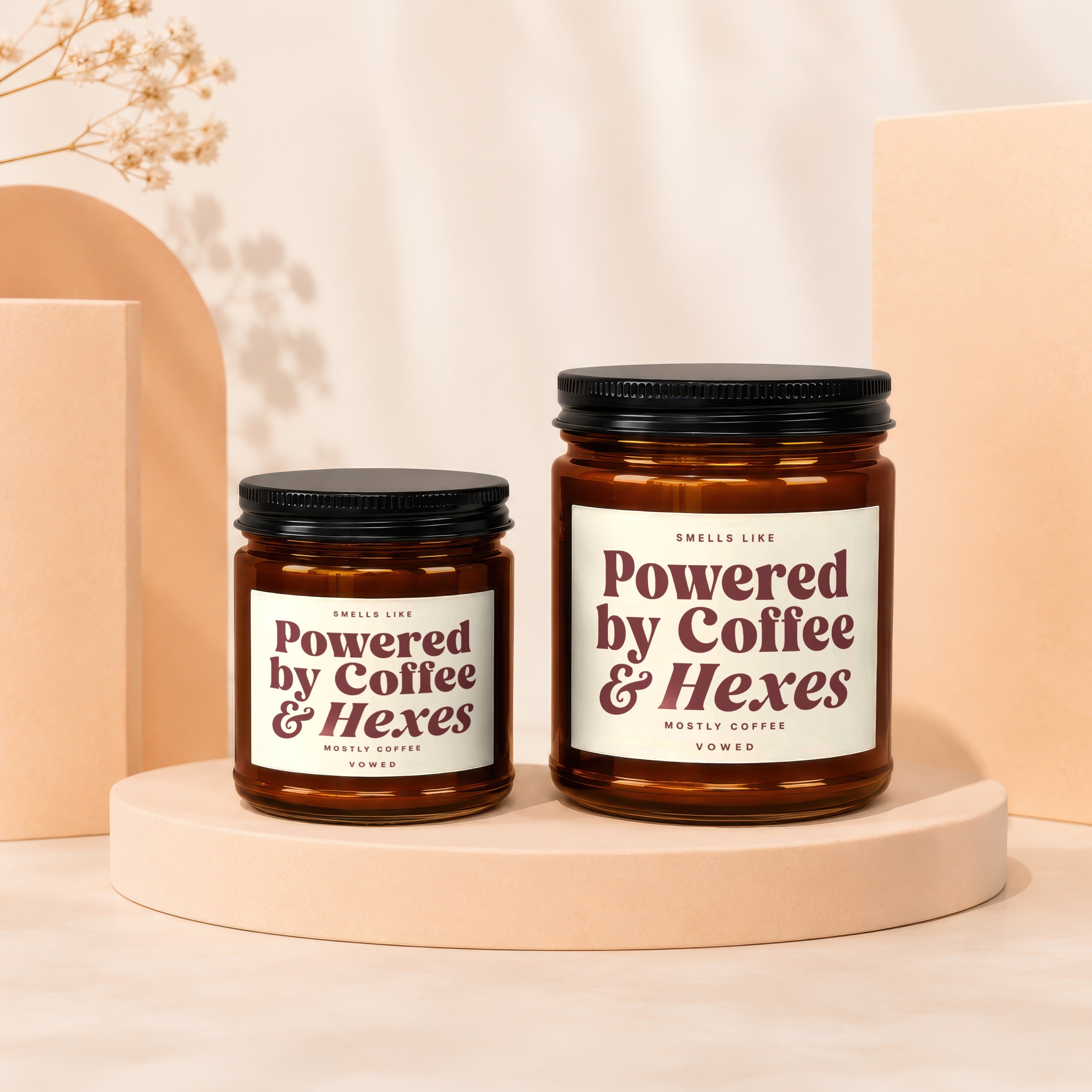 Two amber glass candles with black lids labeled "Powered by Coffee & Hexes".