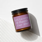 Amber glass candle with purple label reading "Love, Laughter & Happily Ever After".