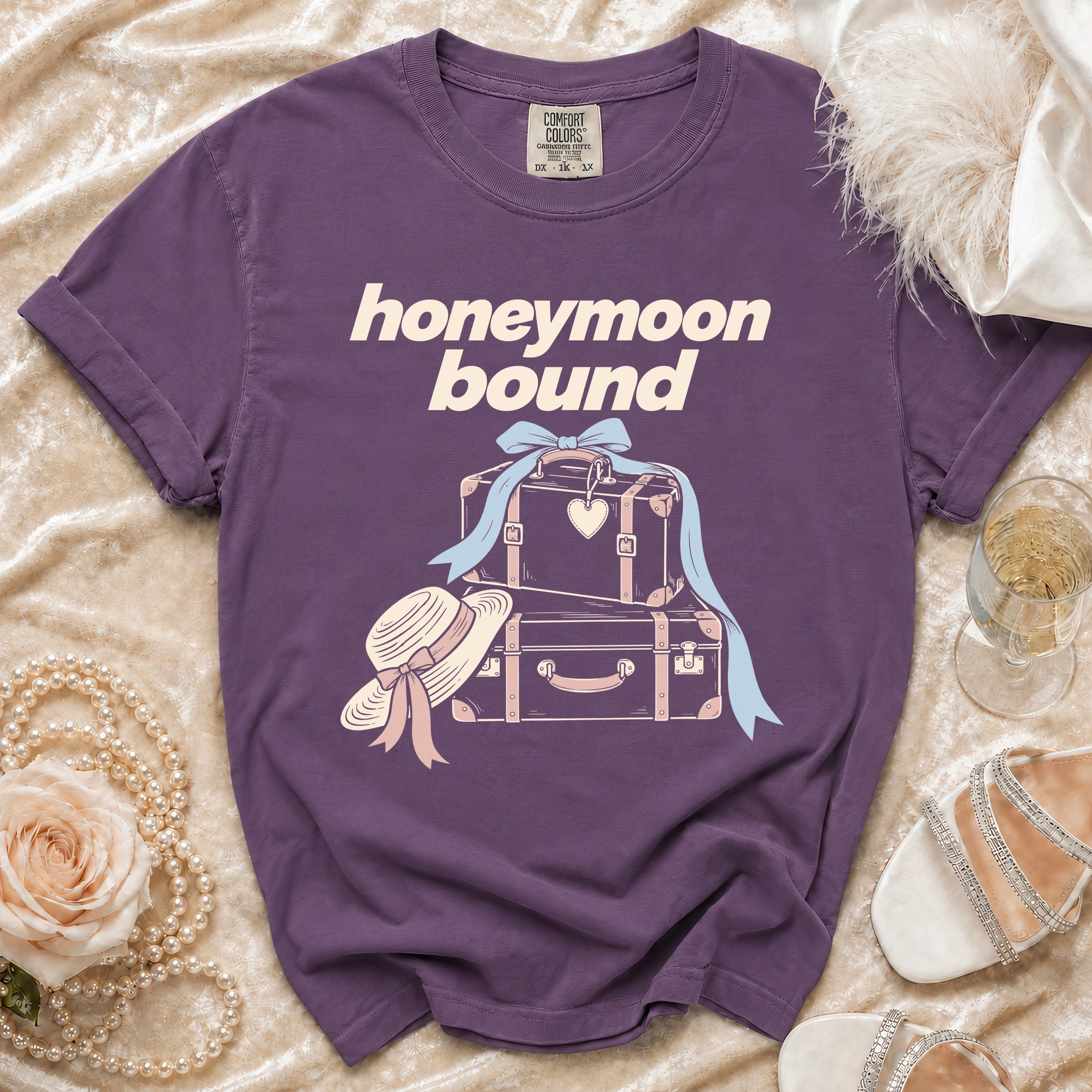 Purple t-shirt with "honeymoon bound" text and graphic of suitcases, hat, and ribbon.