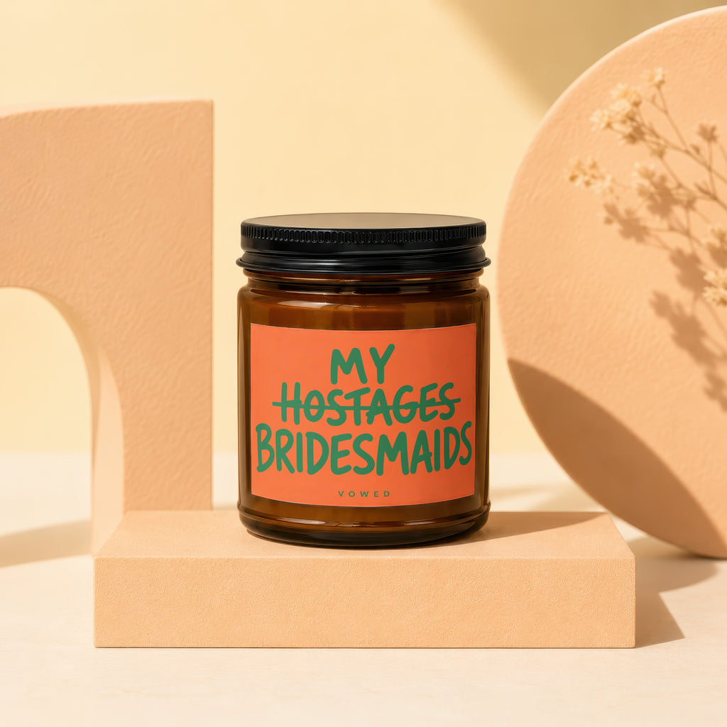 Amber jar candle with orange label reading "MY HOSTAGES BRIDESMAIDS" and "VOWED".