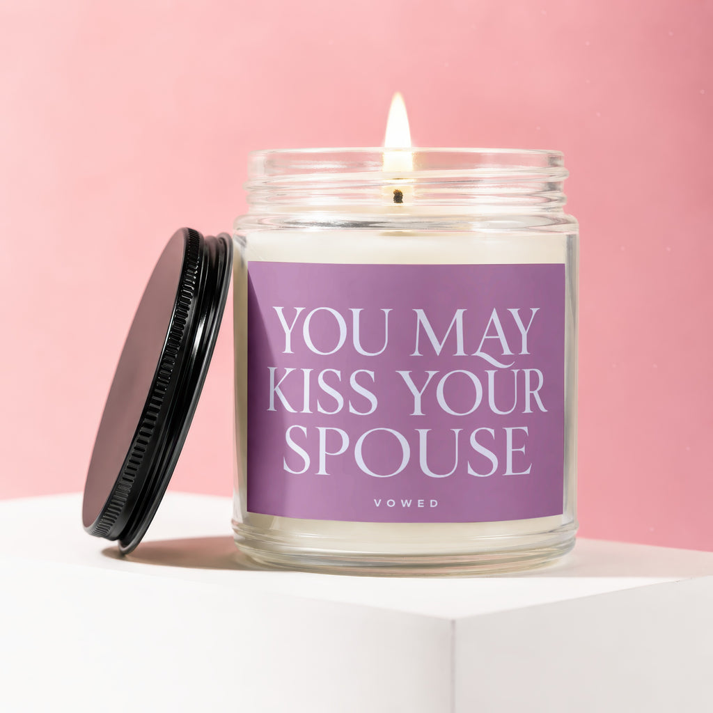 Jar candle with "You May Kiss Your Spouse" text on lavender label, lit wick.
