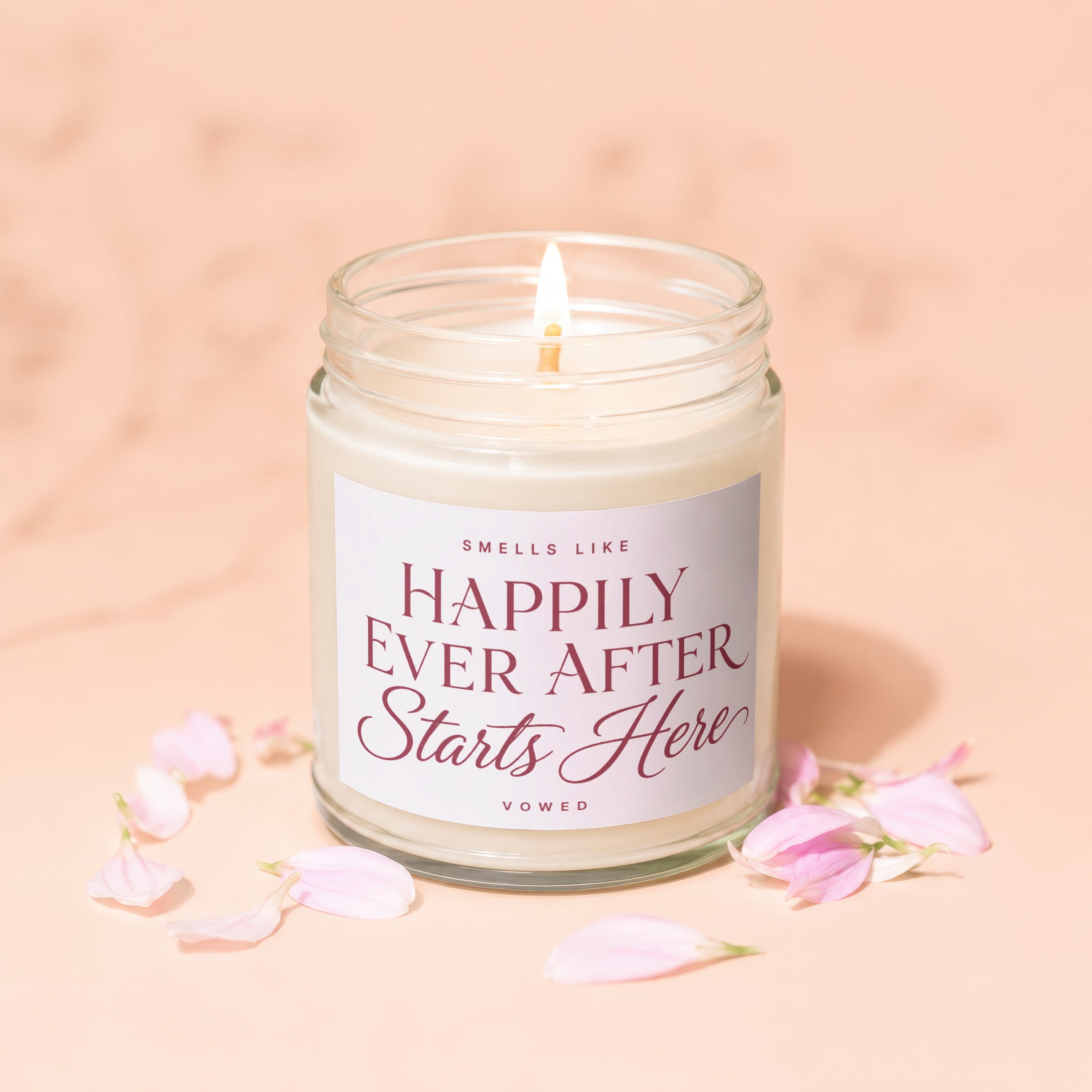 Lit candle in glass jar with "Happily Ever After Starts Here" text and pink petals.