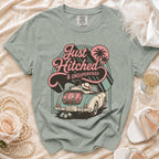 T-shirt graphic of couple in convertible with luggage, "Just Hitched & Unsupervised" text.