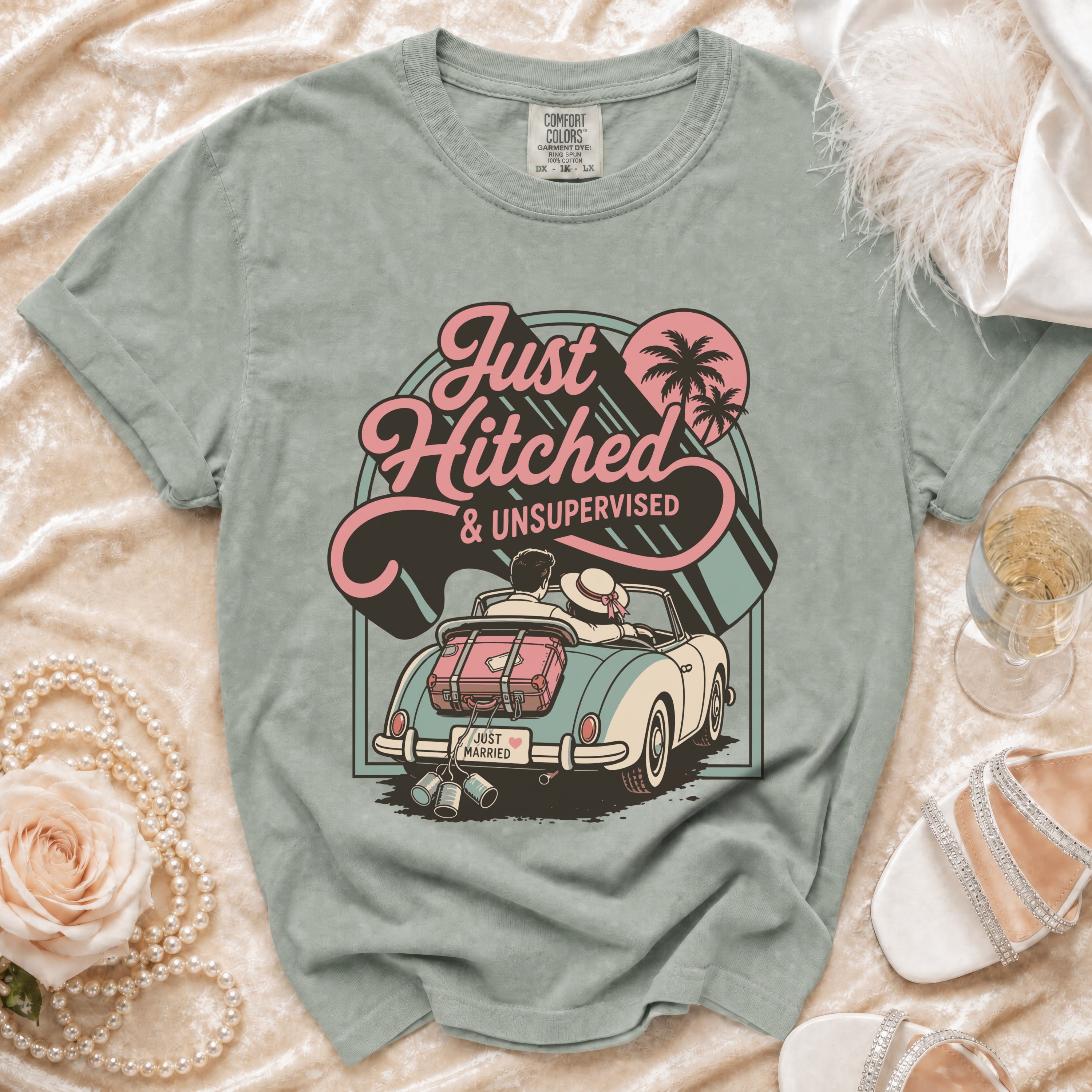 T-shirt graphic of couple in convertible with luggage, "Just Hitched & Unsupervised" text.