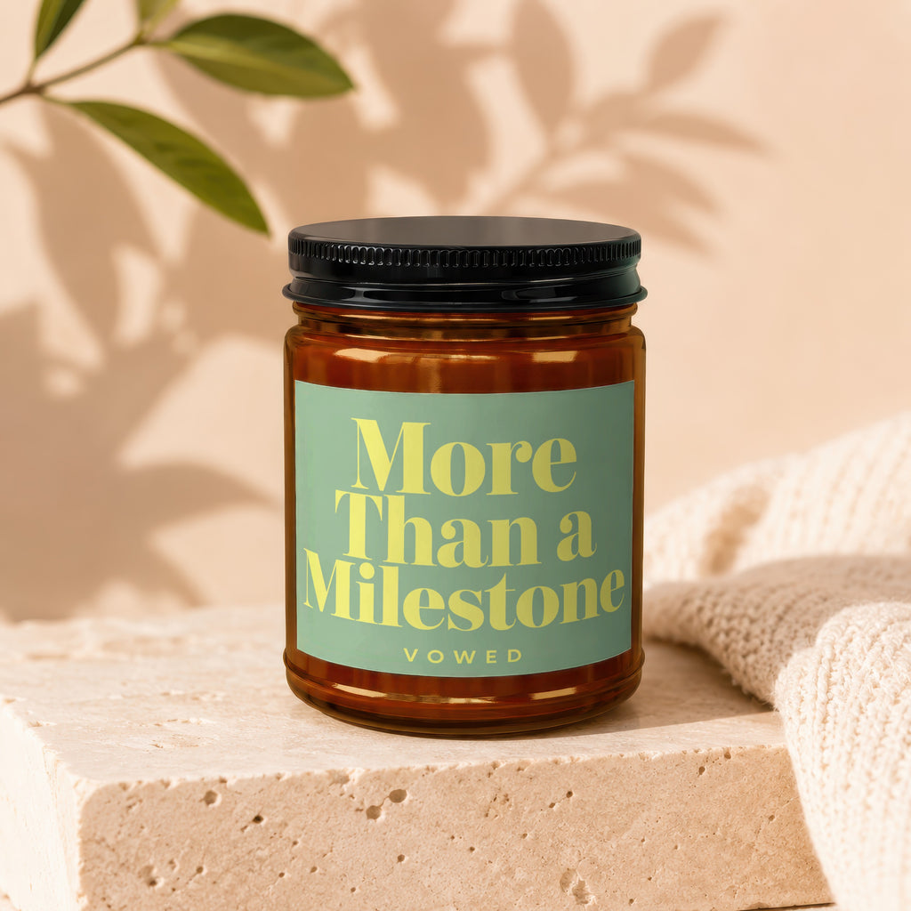 Amber glass candle with green label, reading "More Than a Milestone Vowed".