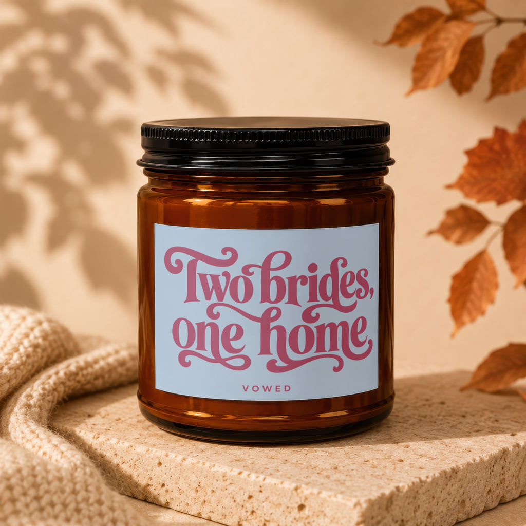 Amber candle with pink text "Two brides, one home" and "VOWED" on label.