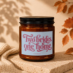 Amber candle with pink text "Two brides, one home" and "VOWED" on label.
