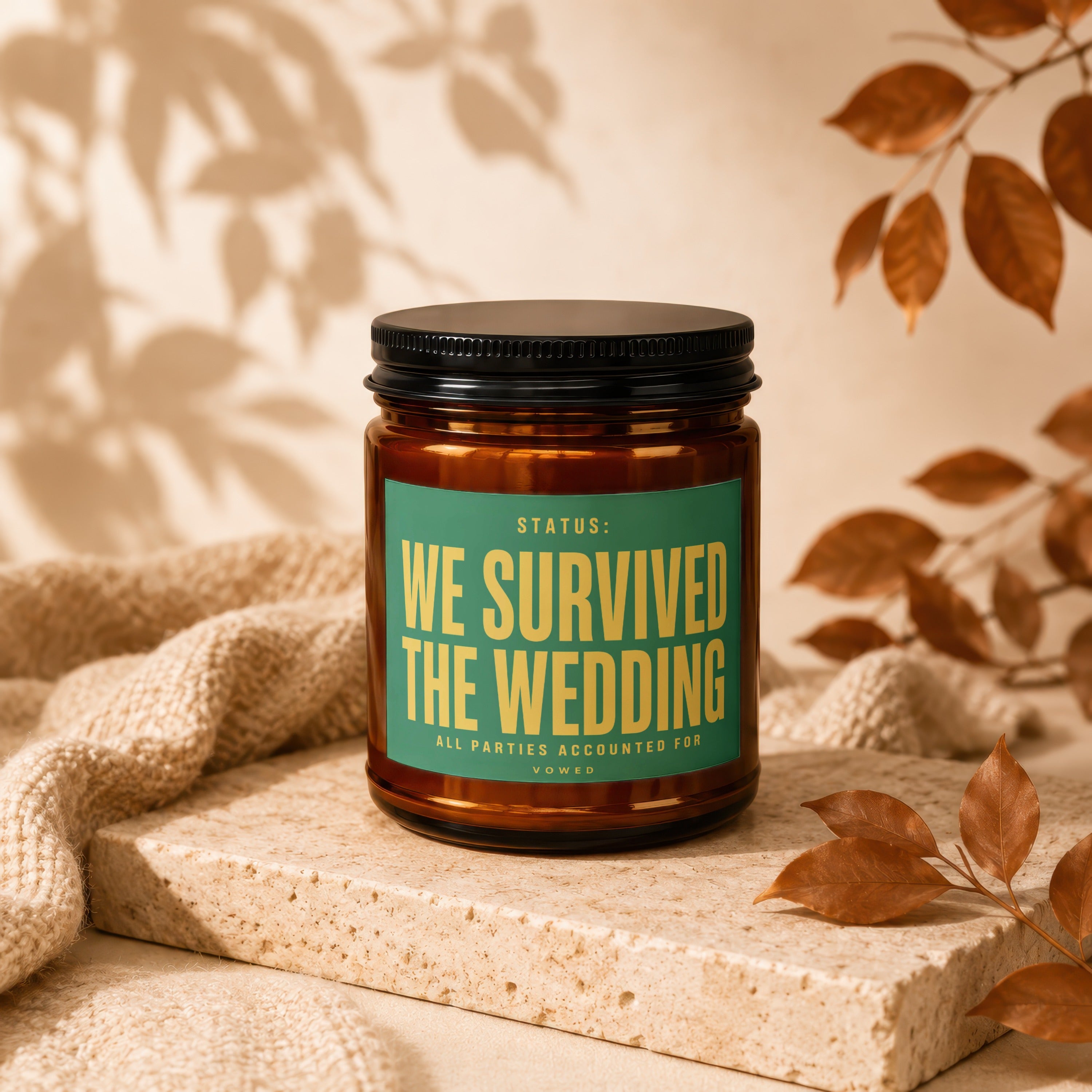 Amber jar candle with green label reading "STATUS: WE SURVIVED THE WEDDING"