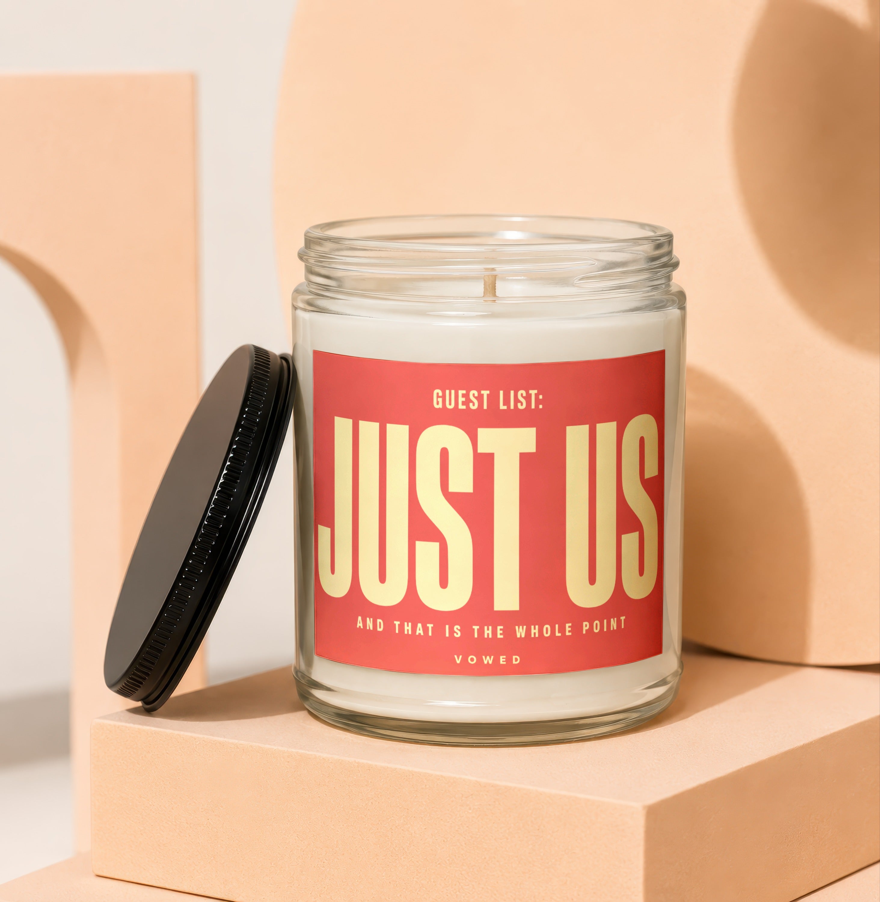 Glass candle with red label reading "GUEST LIST: JUST US" and "VOWED".