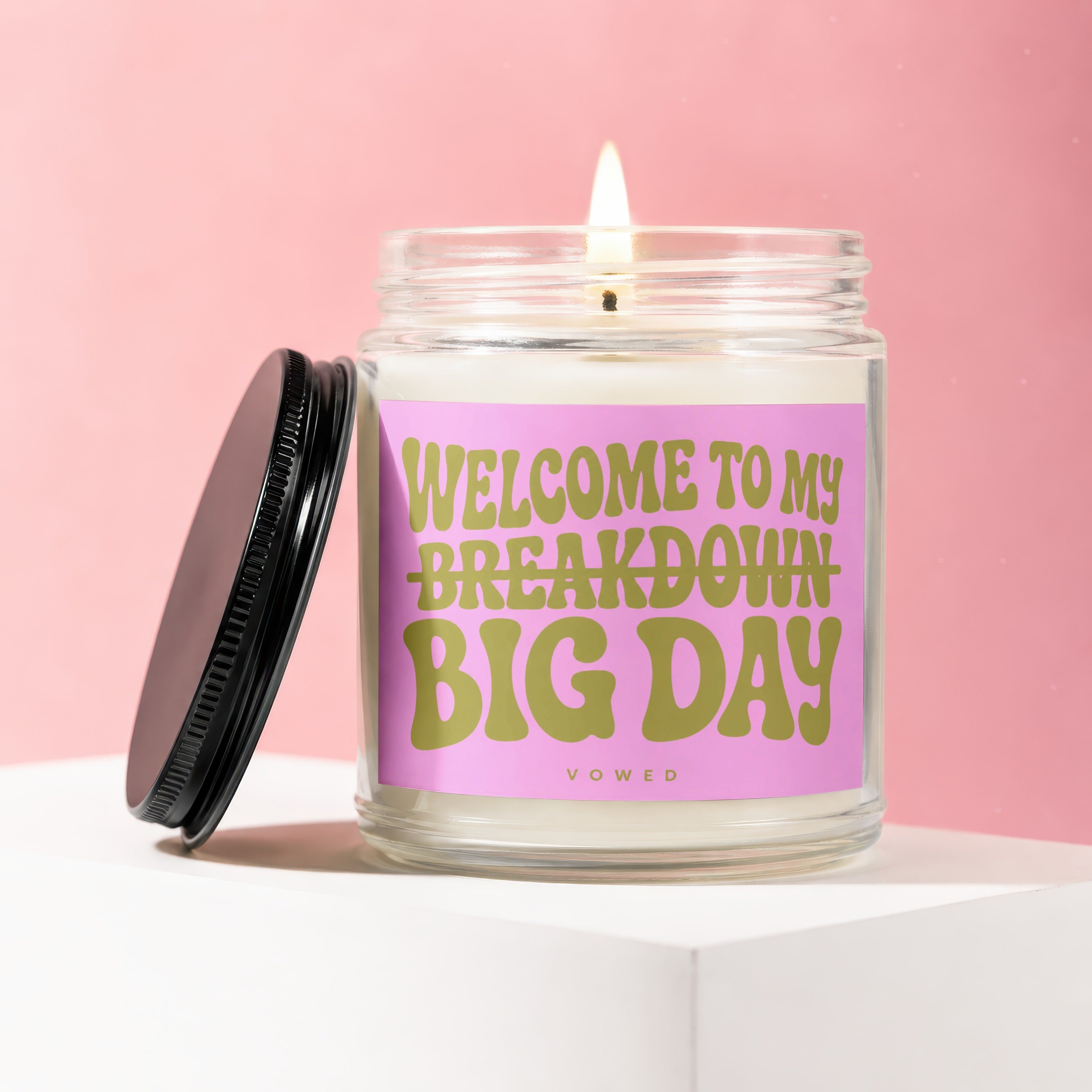 Lit glass candle with pink label reading "WELCOME TO MY BREAKDOWN BIG DAY"