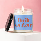 Lit candle in a glass jar with the text "Built on Love VOWED" on a blue label.