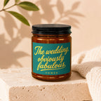 Amber jar candle with dark lid, teal label reads "The wedding, obviously fabulous."