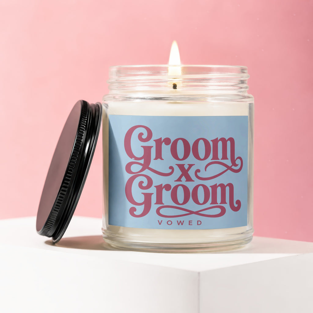 Candle with "Groom x Groom Vowed" text on blue label with a lit wick.