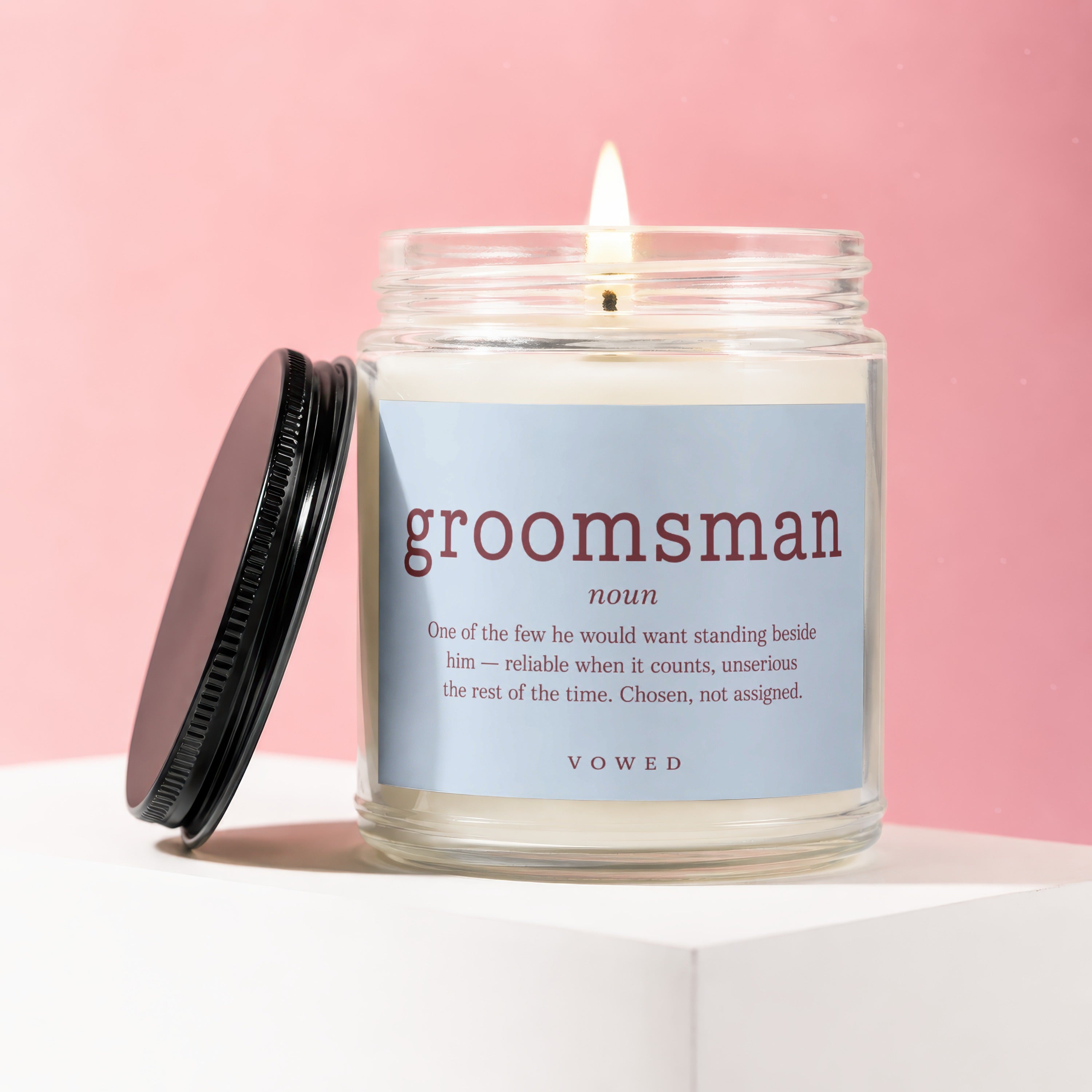 Glass candle labeled "groomsman" with a definition, on a pink background.