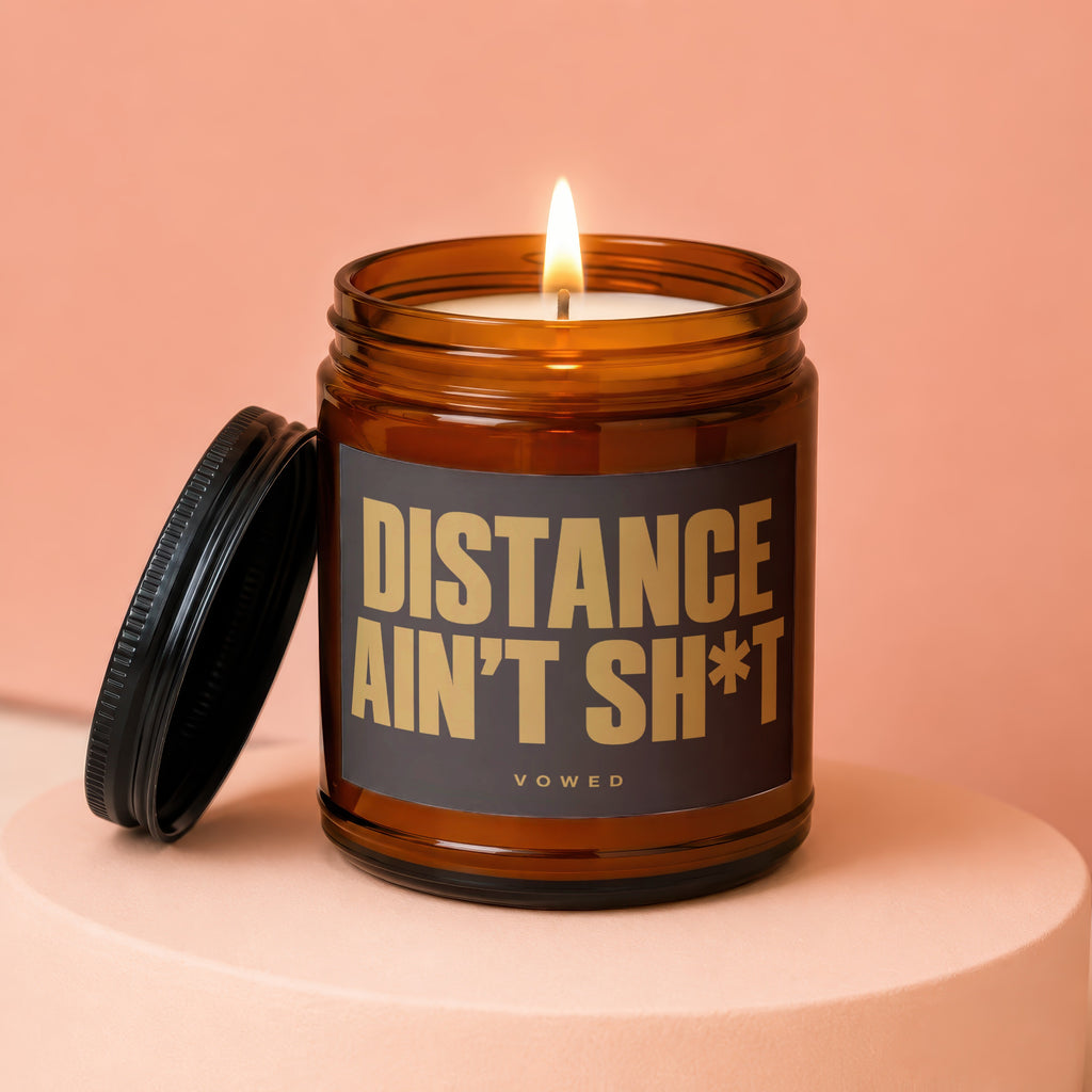 Amber jar candle with lit wick and black lid, reads "DISTANCE AIN'T SH*T VOWED".