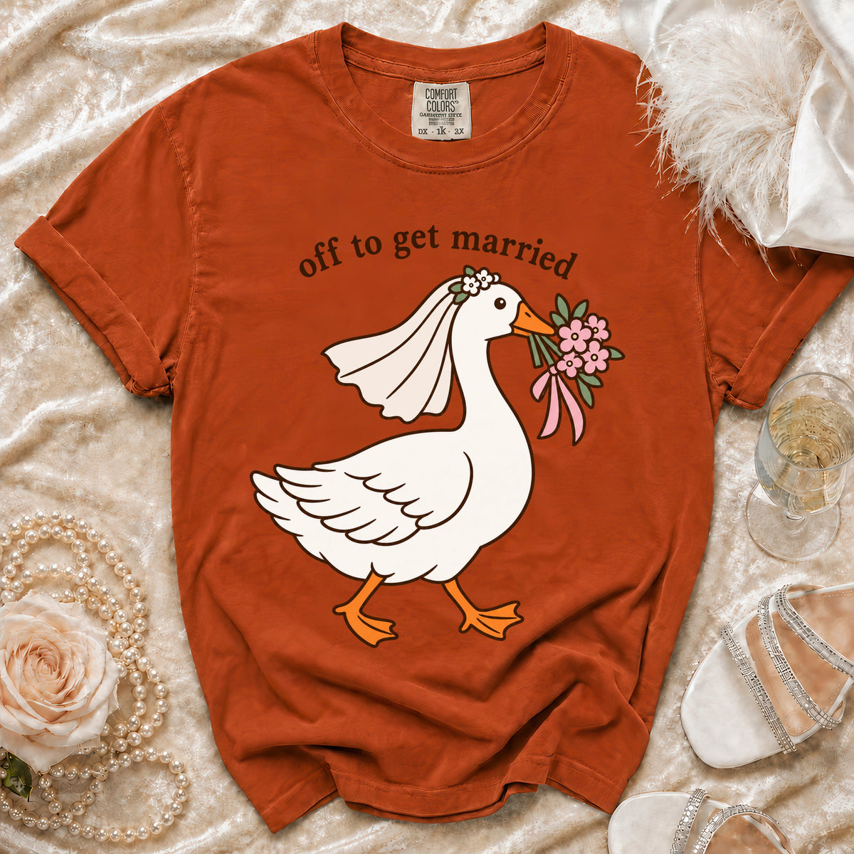 Orange t-shirt with graphic of goose in wedding veil holding flowers, text "off to get married".