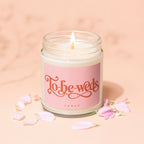 Candle with lit wick, pink label reading "To-be-weds" and "VOWED", surrounded by petals.