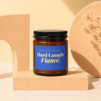 Amber jar candle with blue label reading "Hard Launch: Fiancé."