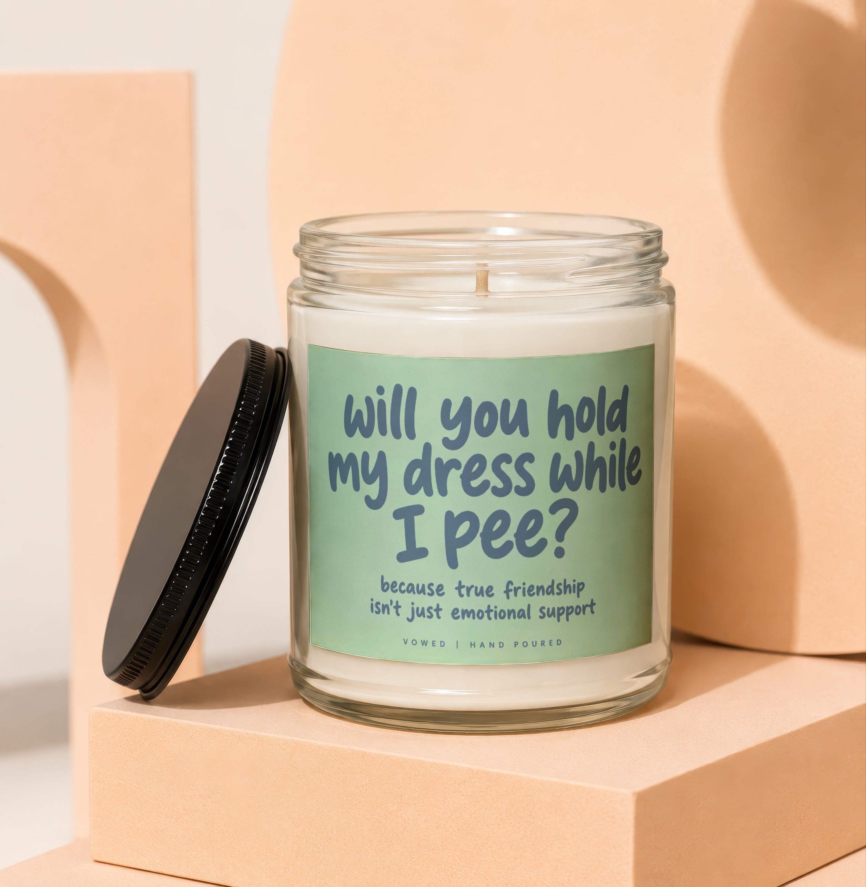 Glass candle with label: "will you hold my dress while I pee?", "Vowed | Hand Poured".