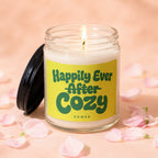 Glass candle with lid off, lit wick, and "Happily Ever After Cozy" text.