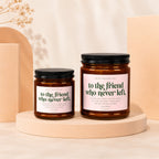 Two amber glass candles with black lids and pink labels. Labels read, "to the friend who never left".