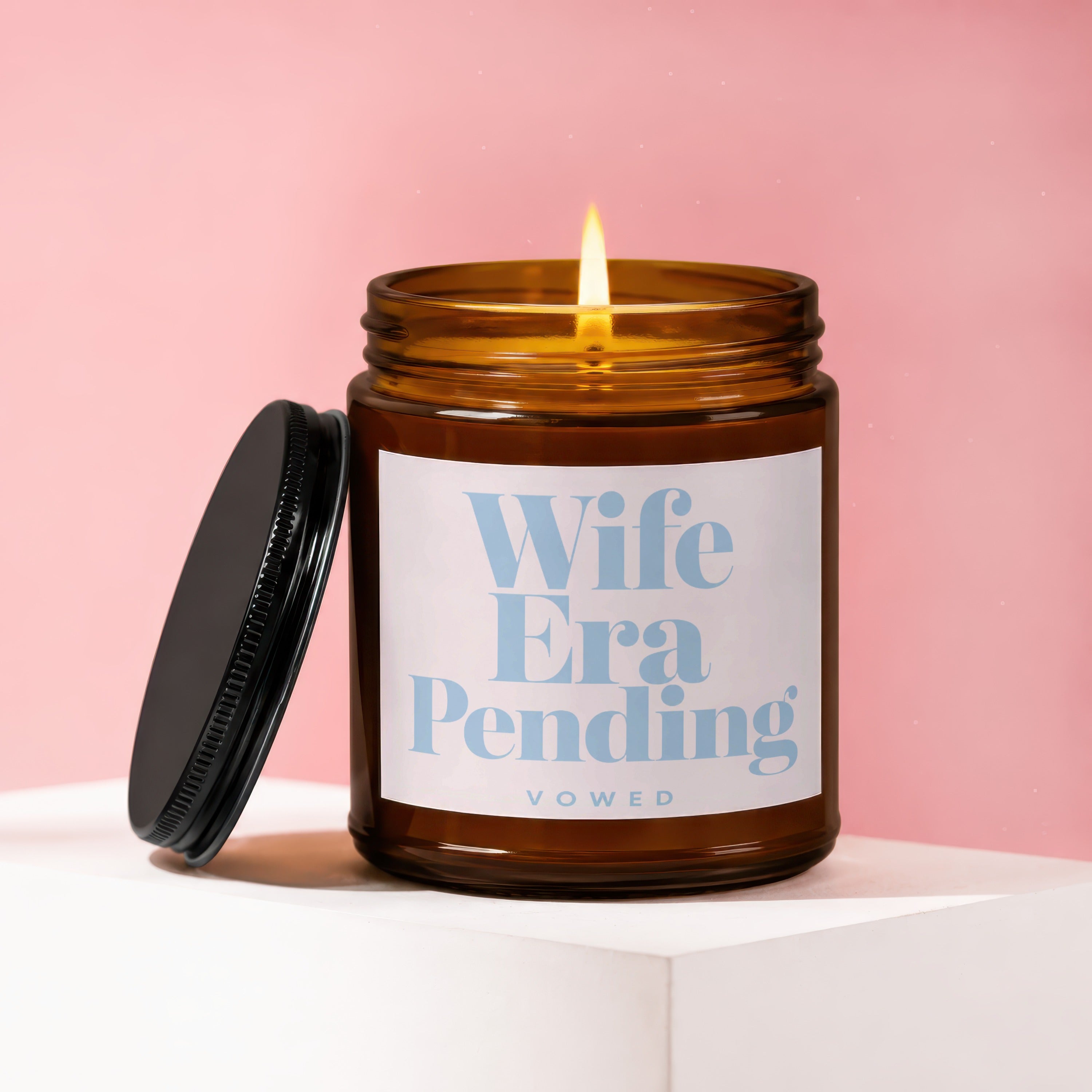 Amber jar candle with lit flame, "Wife Era Pending VOWED" text on label.