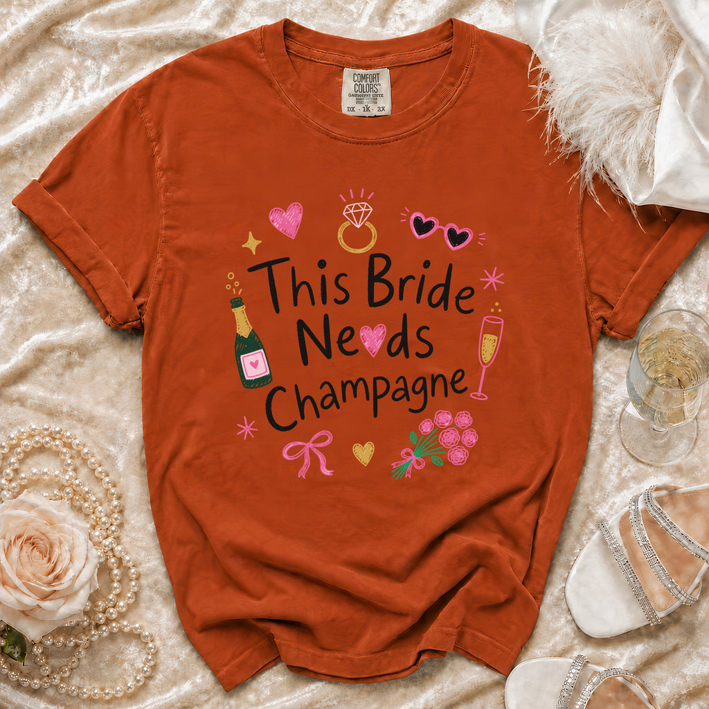Orange t-shirt with "This Bride Needs Champagne" graphic and bridal accessories.