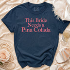 Navy Comfort Colors t-shirt with pink text "This Bride Needs a Pina Colada".