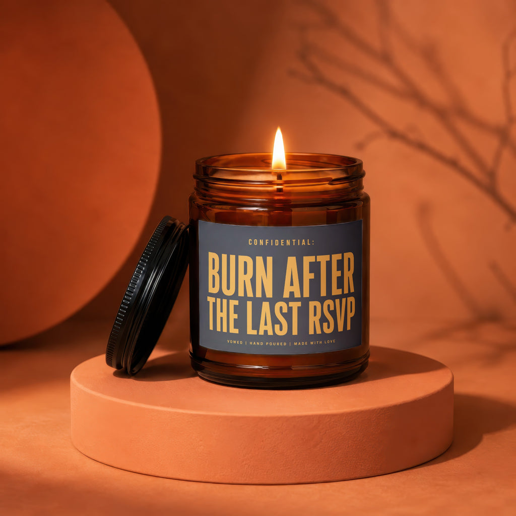 Amber candle with a lit flame and dark lid, reads "Burn After The Last RSVP."
