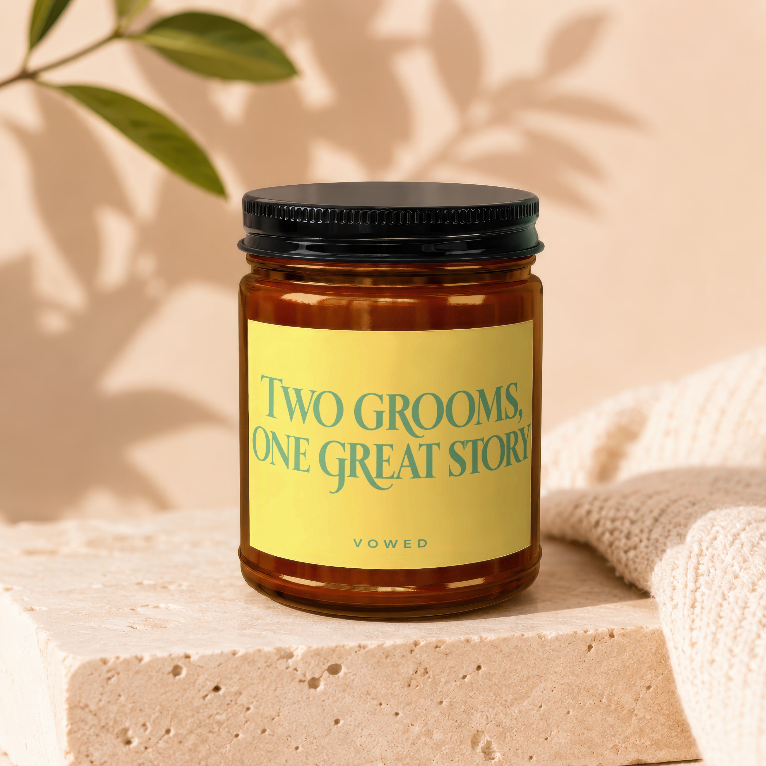 Amber candle in a jar with a black lid and a yellow label reading "TWO GROOMS, ONE GREAT STORY VOWED".