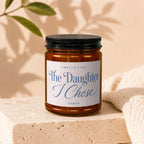 Glass candle with black lid, white label reads "Smells Like The Daughter I Chose".