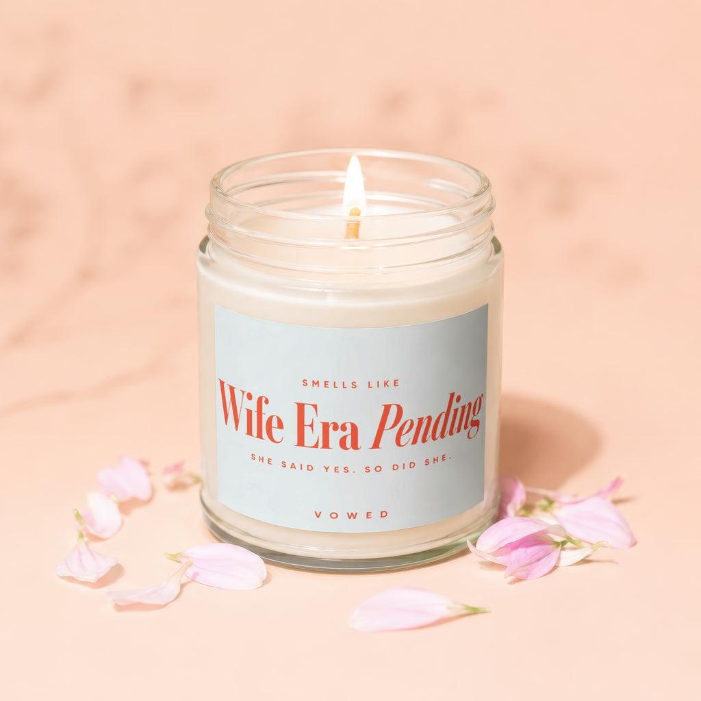 Glass candle with lit wick, label reads "Wife Era Pending".