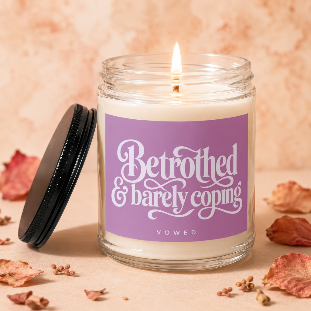 Lit candle in a jar with purple label reading "Betrothed & barely coping" and "VOWED".
